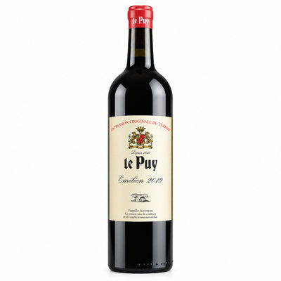 A bottle of te Puy Crémant de Bourgogne sparkling wine with a cream-colored label and a red foil top, standing on a wooden table with a blurred wine shop background.